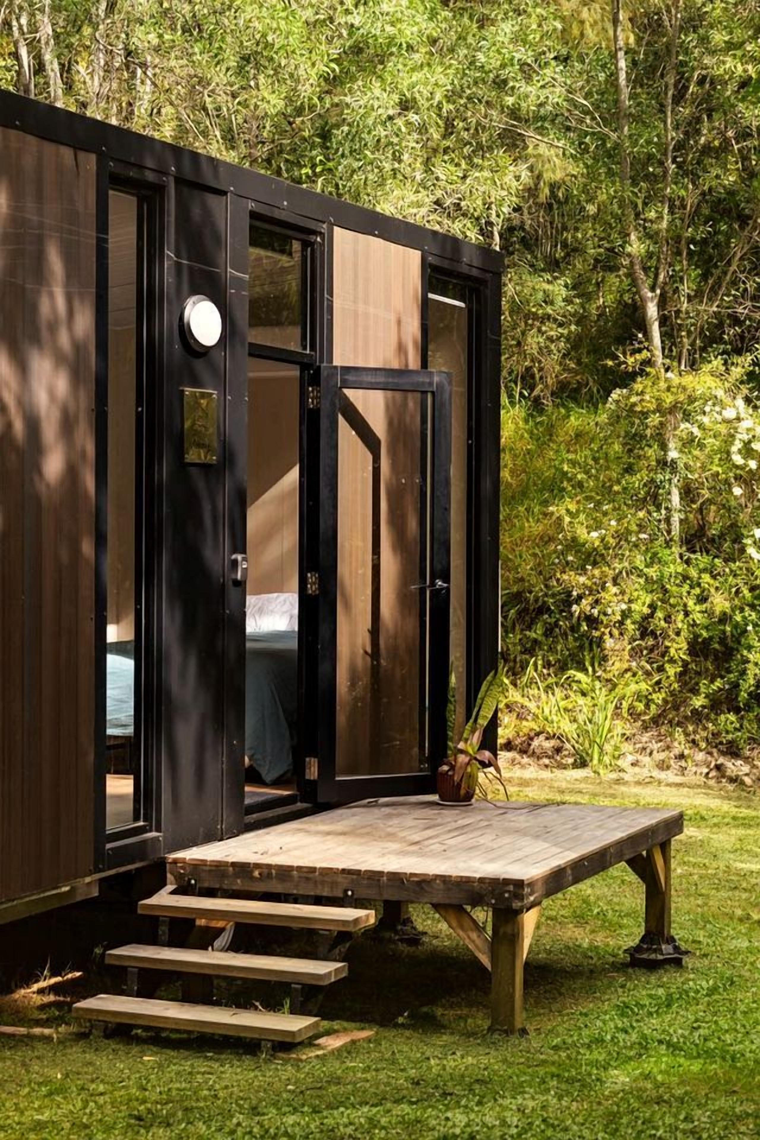 Eine kompakte, moderne Holzhütte mit Glastüren, eingebettet in eine üppige, grüne Landschaft.