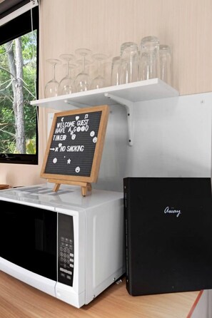 A kitchen area with a microwave, a chalkboard sign, and a shelf with wine glasses.