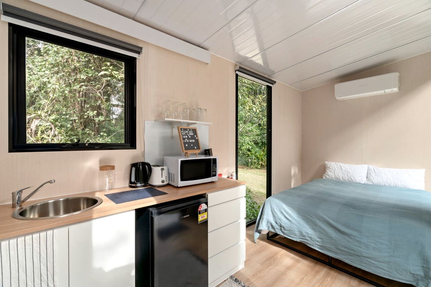 Quarto compacto com cozinha compacta, uma cama e vista para o verde lá fora.