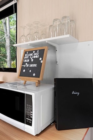 Una cocina con microondas, un letrero de pizarra y una repisa con copas de vino.