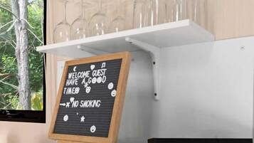 A kitchen area with a microwave, a chalkboard sign, and a shelf with wine glasses.