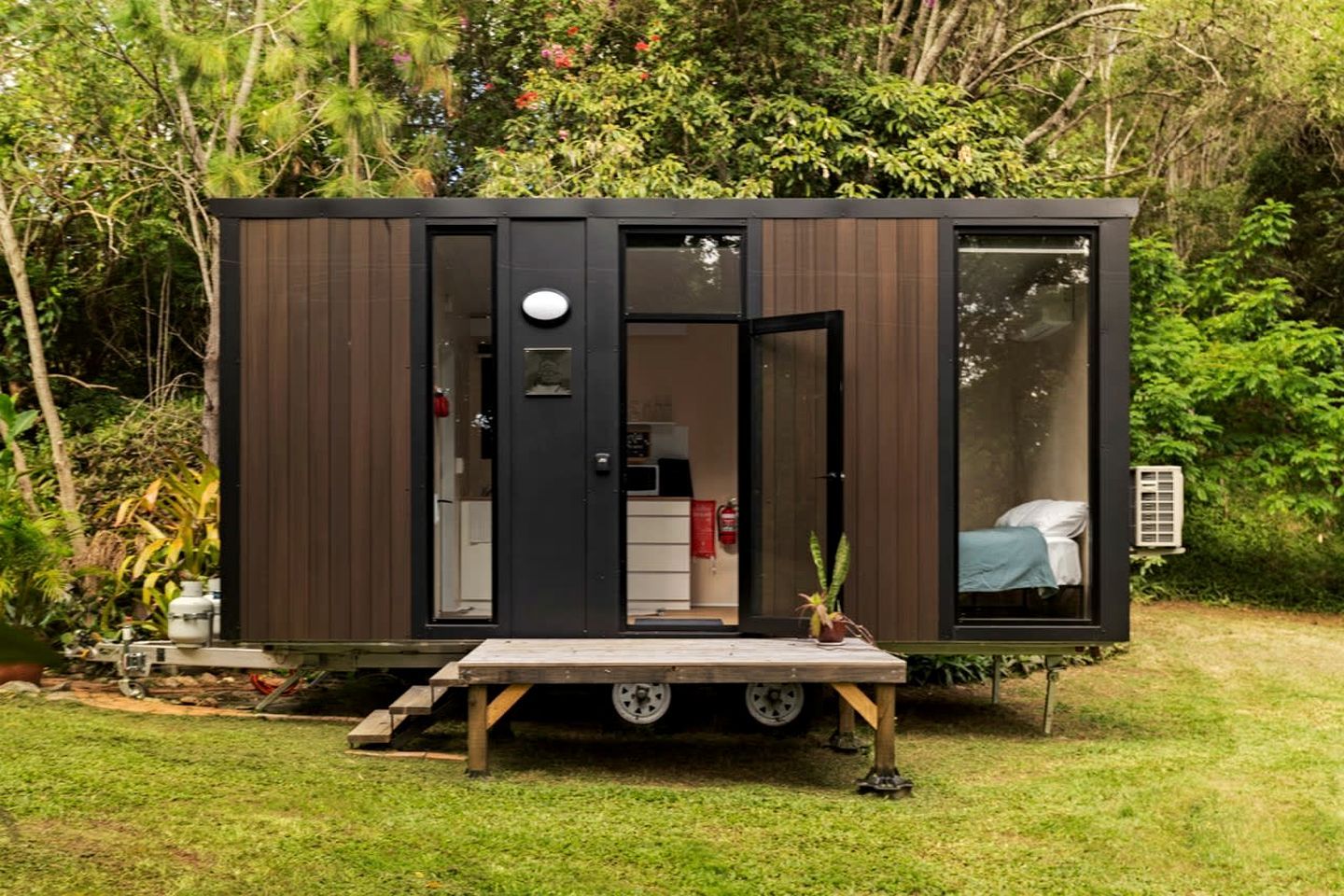 Uma casa móvel moderna e compacta, com um pequeno alpendre, cama e cozinha compacta.