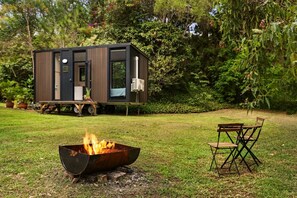 Una casa moderna y compacta con un brasero en primer plano y una terraza amueblada al aire libre.