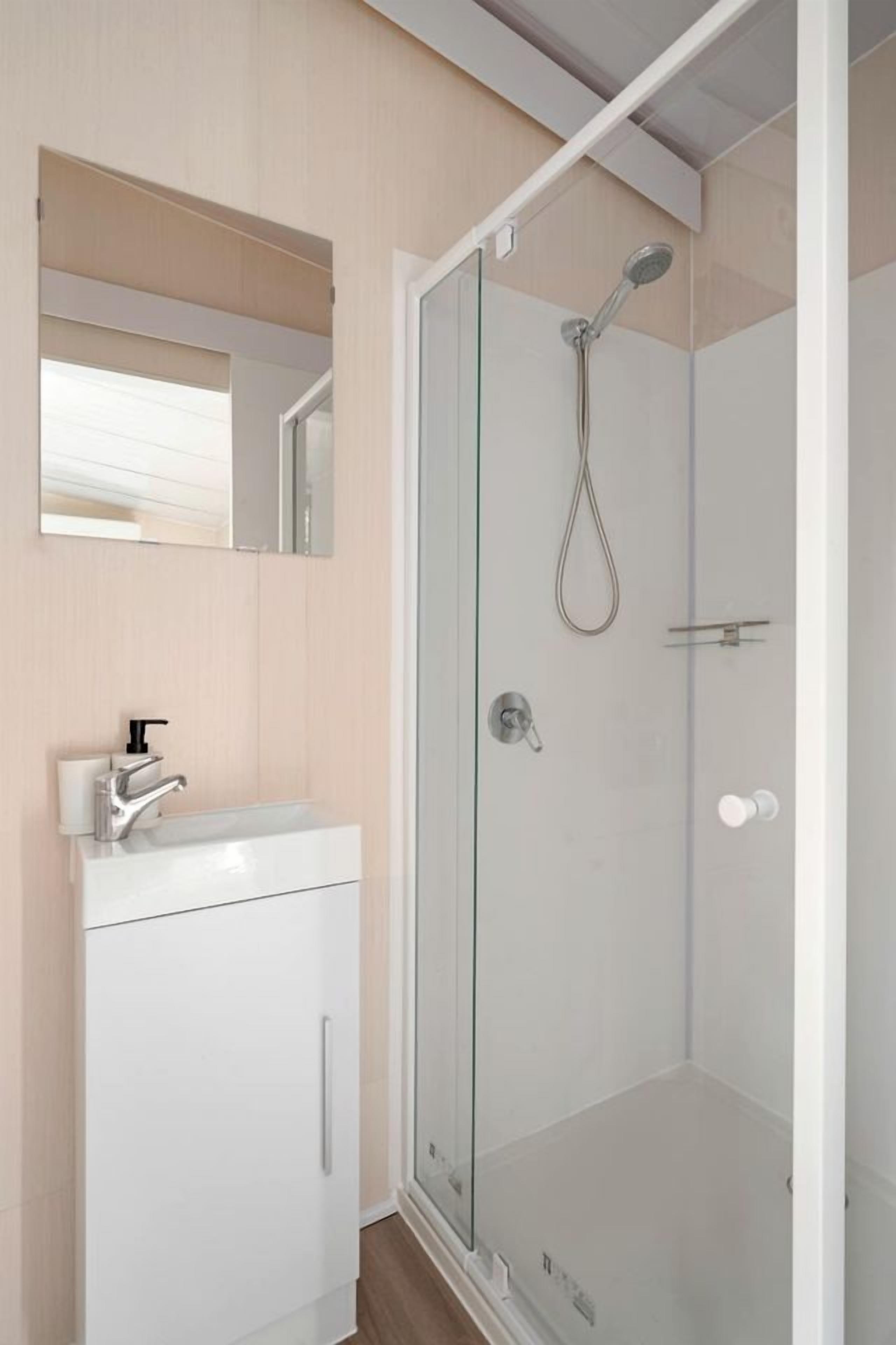 Une salle de bain moderne avec une douche à parois de verre, un lavabo blanc avec un robinet et un miroir au-dessus du lavabo.