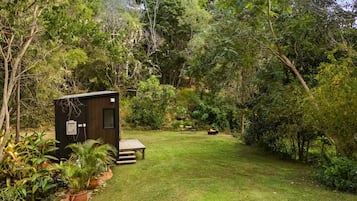 Une petite construction en bois, avec un banc et un foyer, située dans un jardin luxuriant.
