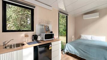 Een compacte kamer met een kitchenette, een bed en uitzicht op groen.
