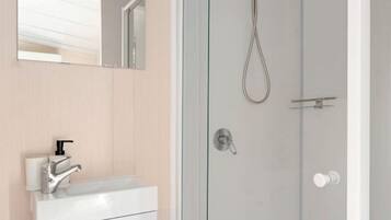 Une salle de bain moderne avec une douche à parois de verre, un lavabo blanc avec un robinet et un miroir au-dessus du lavabo.