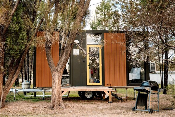 A small, portable structure with a door, a bench, and a grill outside.