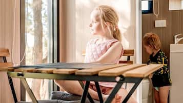 A room with a dining table, a cushioned chair, and a child playing near a window.