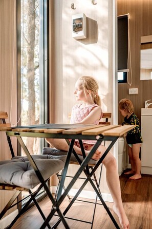 Una habitación con una mesa de comedor, un sillón acolchado y un niño jugando cerca de una ventana.