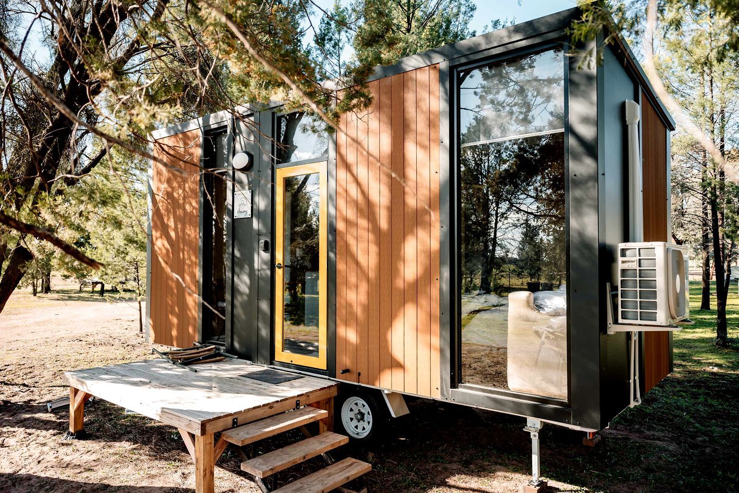A small, modern mobile home with a sliding door, a small porch, and a window.