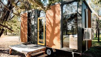 A small, modern mobile home with a sliding door, a small porch, and a window.