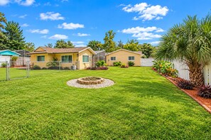 A residential property with a well-maintained lawn, a circular fire pit, and a white fence.