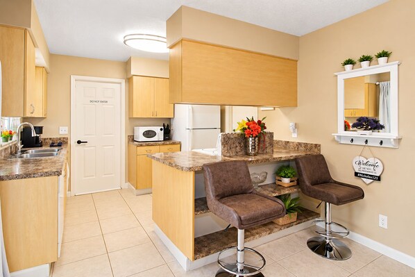 A compact kitchen with a built-in island, bar stools, and a microwave.