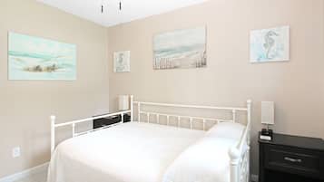 A bedroom with a white bed, a nightstand, and a dresser. There are three paintings on the wall.