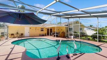 A swimming pool with a glass enclosure, surrounded by a patio area with chairs and a table.