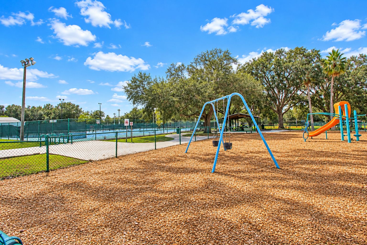 Un'area giochi con altalene e scivolo, circondata da alberi e recintata.