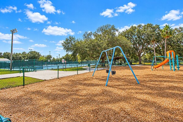 A playground with swings and a slide, surrounded by trees and a fenced area.
