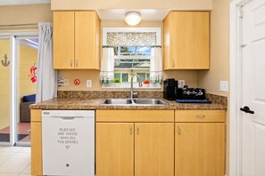 A compact kitchen with a dishwasher, a coffee maker, and a window with a decorative curtain.