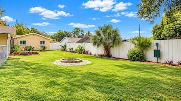 A well-maintained backyard with a circular fire pit, a white fence, and a variety of plants.