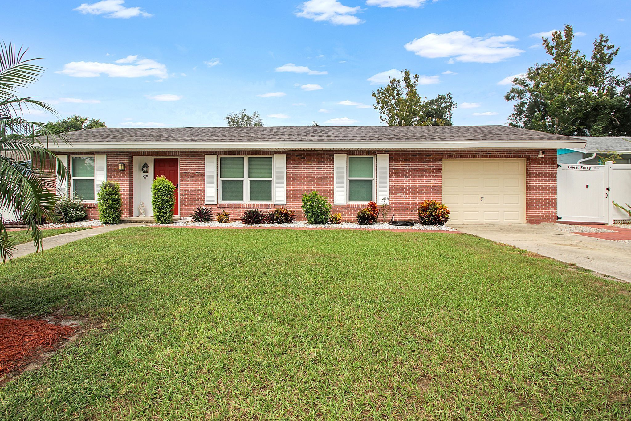 A single-story brick house with a front yard, a garage, and a guest entry gate.