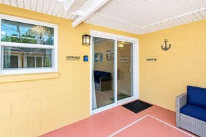 A yellow-walled room with a glass door entrance, a blue sofa, and a sign indicating 'UNIT #2'.