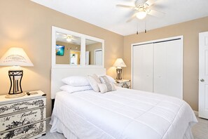 A bedroom with a bed, a dresser, a mirror, a ceiling fan, and a door.