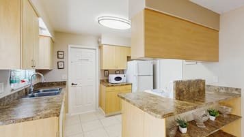 A compact kitchen with a microwave, refrigerator, and granite countertops.