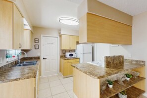 A compact kitchen with a microwave, refrigerator, and granite countertops.