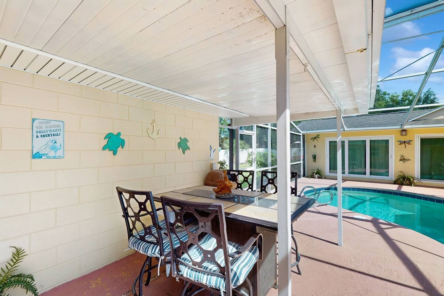 An outdoor patio with a pool, a covered seating area, and a wall with decorative elements.
