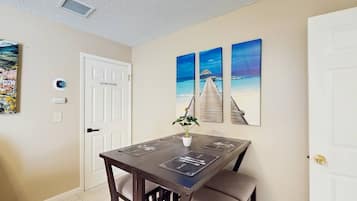 A dining area with a table and chairs, a door with a 'DO NOT ENTER' sign, and three beach-themed wall art pieces.