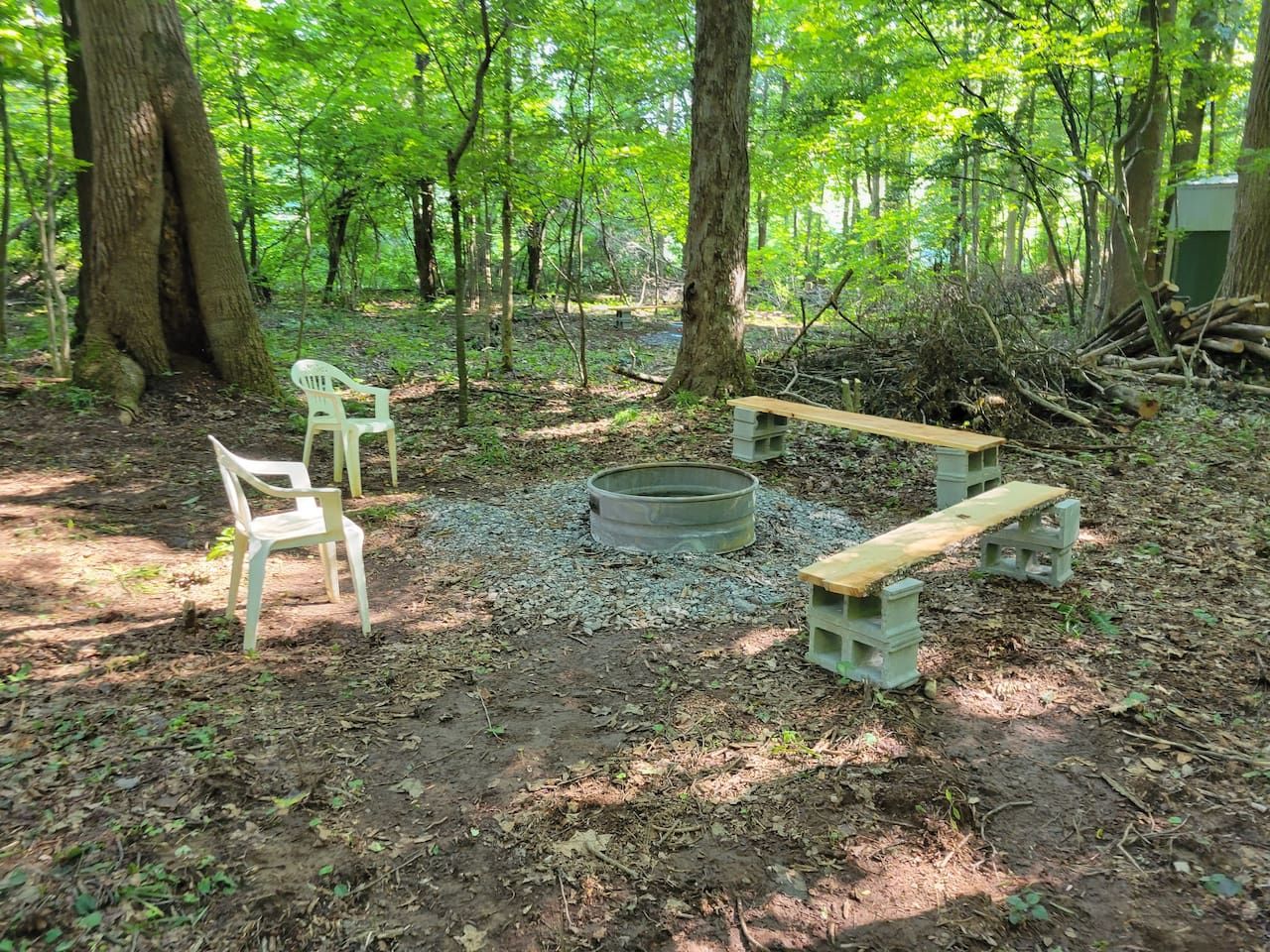 An outdoor seating area with benches and chairs, surrounded by trees.