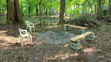 An outdoor seating area with benches and chairs, surrounded by trees.