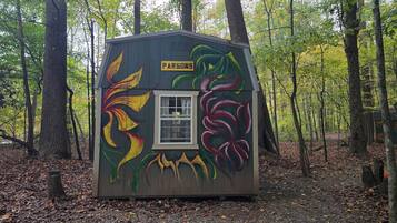 Una piccola baita di legno con una finestra e una porta, circondata da alberi e decorata con motivi a foglie colorate.