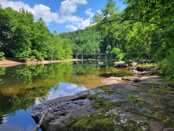 A natural landscape with a calm river, rocky shore, and dense forest.