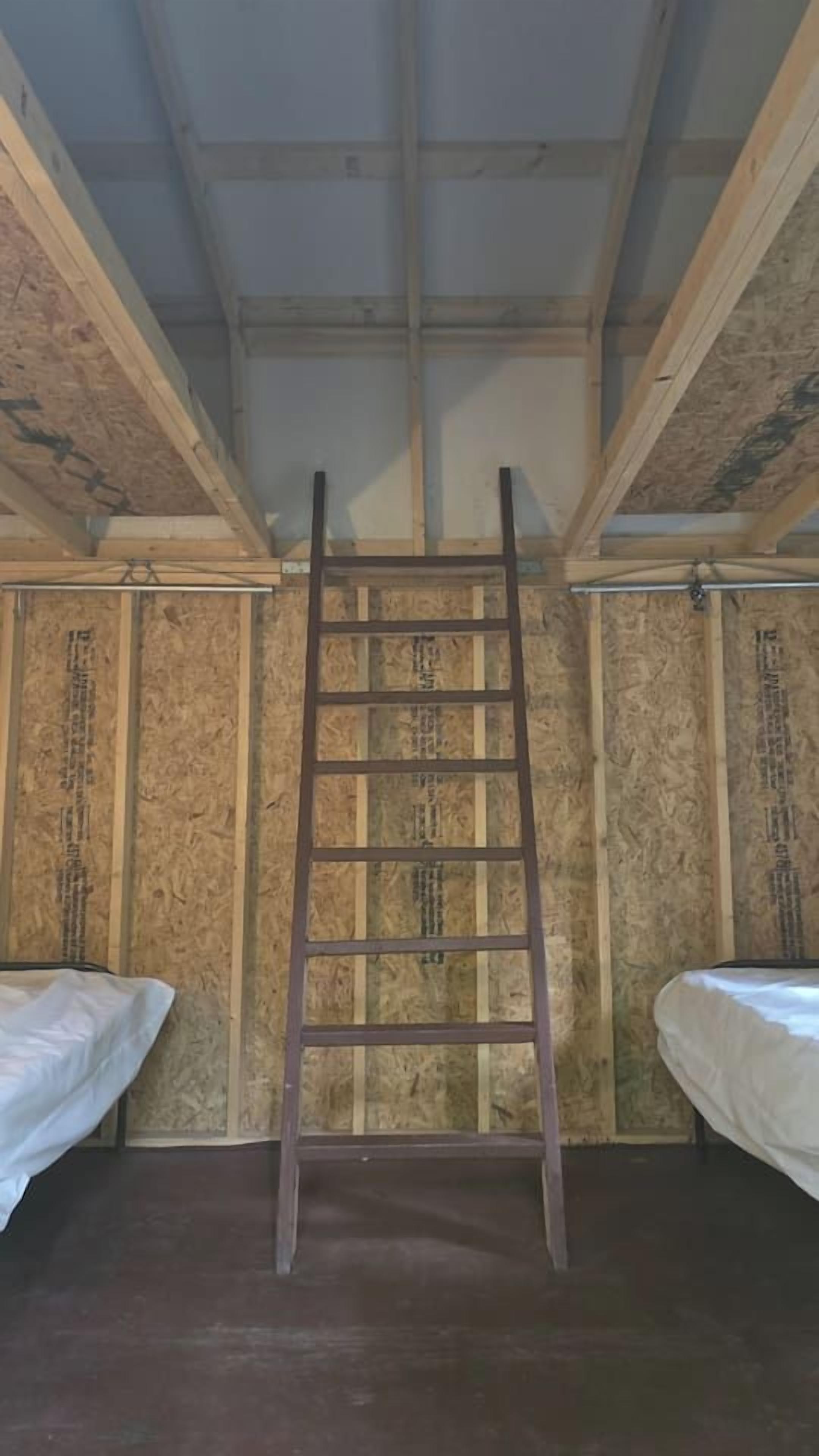 Ein Zimmer mit einer Holzleiter an der Wand, zwei Betten mit weißer Bettwäsche und Holzvertäfelung.