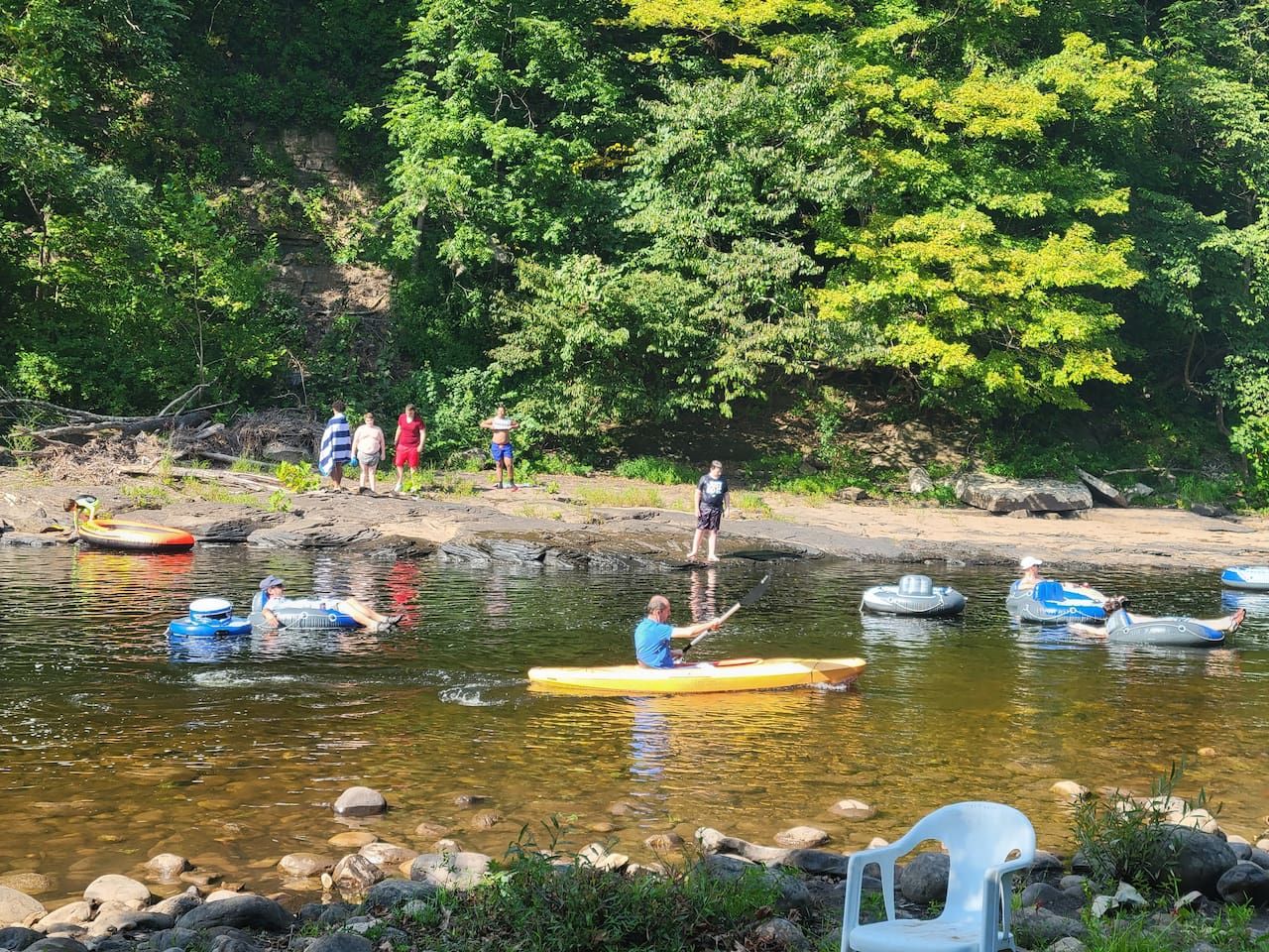 A river with people in inflatable boats and a few standing on the bank.