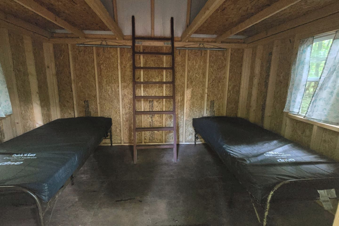 A room with two bunk beds, a ladder, wooden walls, and a window.