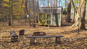 A rustic cabin with a metal roof, surrounded by a forest with fallen leaves on the ground. - The Parsons - Cabin CB1 (Parsons)