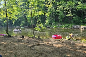 A sandy riverbank with a boat and inflatable rings, surrounded by dense greenery.