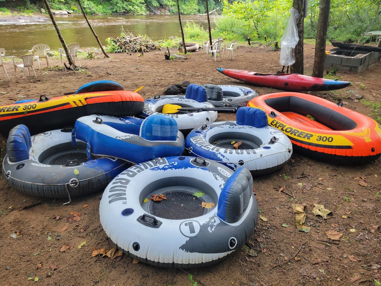 A collection of inflatable rafts on a dirt ground near a body of water.