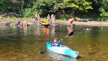 A kayaker in a blue kayak on a calm river with people on the shore.