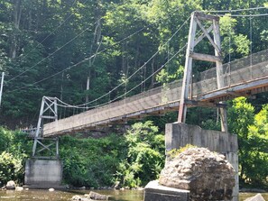 A suspension bridge over a river with dense foliage on both sides. - The Hendricks - Cabin CB3 (Parsons)