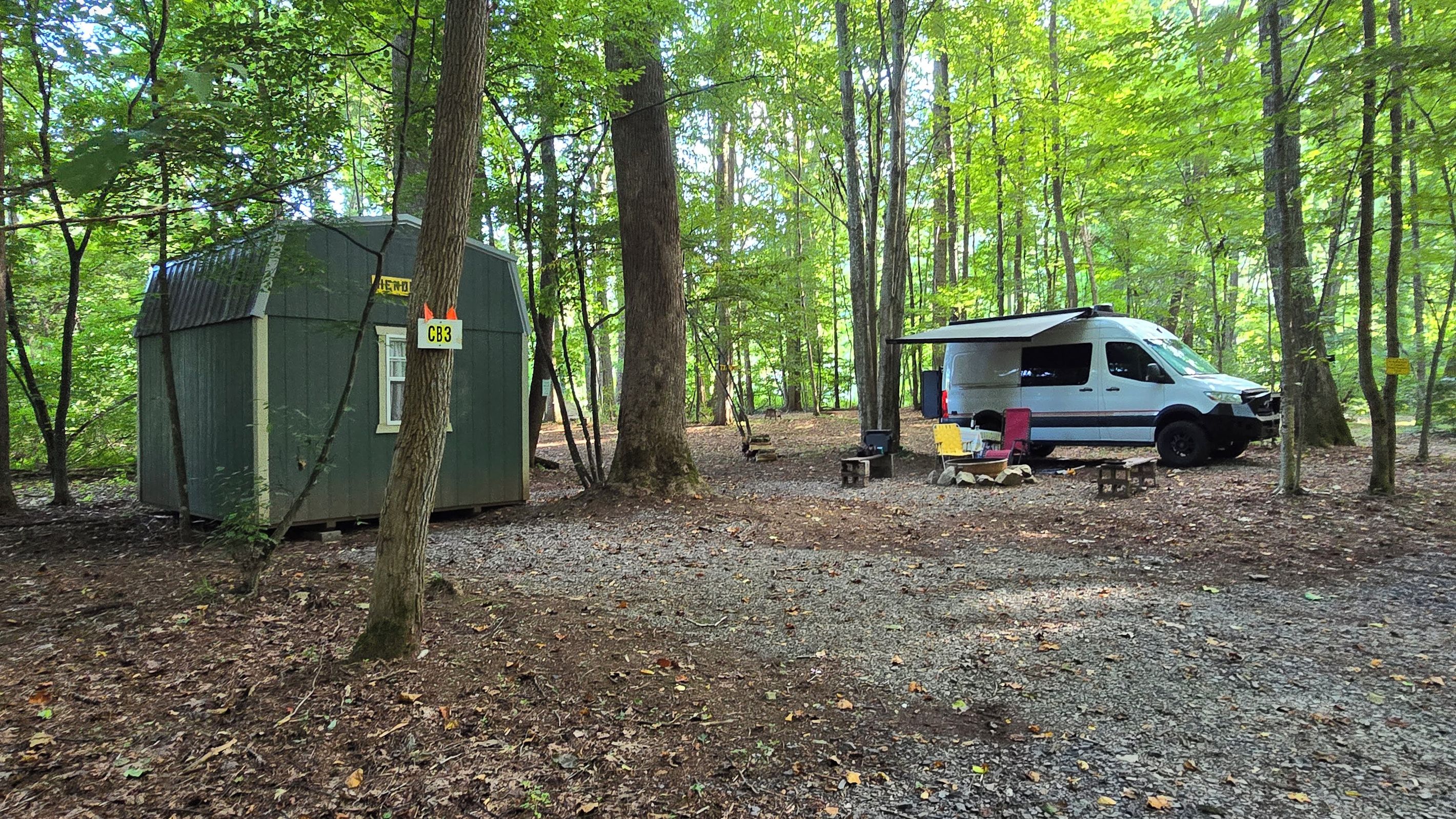 A campsite with a green cabin and a white RV parked in a wooded area.