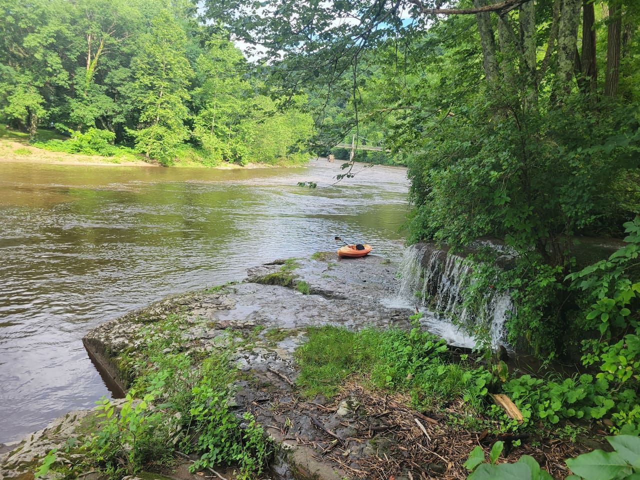 Une rivière avec un petit bateau, une cascade et une végétation luxuriante.