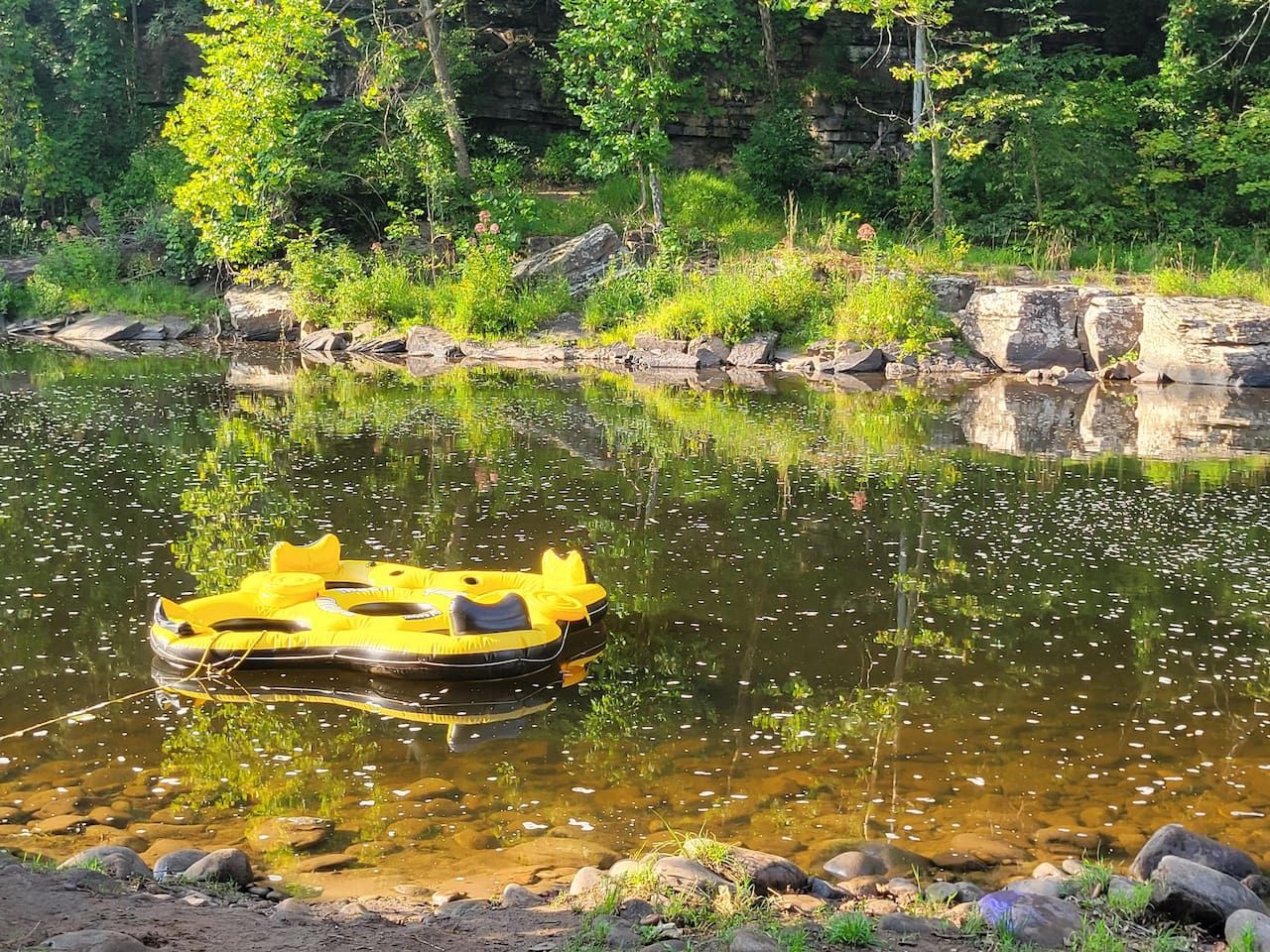 A yellow inflatable raft on a calm river surrounded by rocks and greenery.