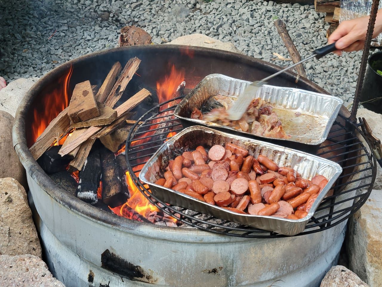 A portable grill with sausages cooking over an open flame.