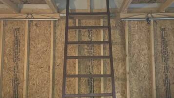 Ein Zimmer mit einer Holzleiter an der Wand, zwei Betten mit weißer Bettwäsche und Holzvertäfelung.