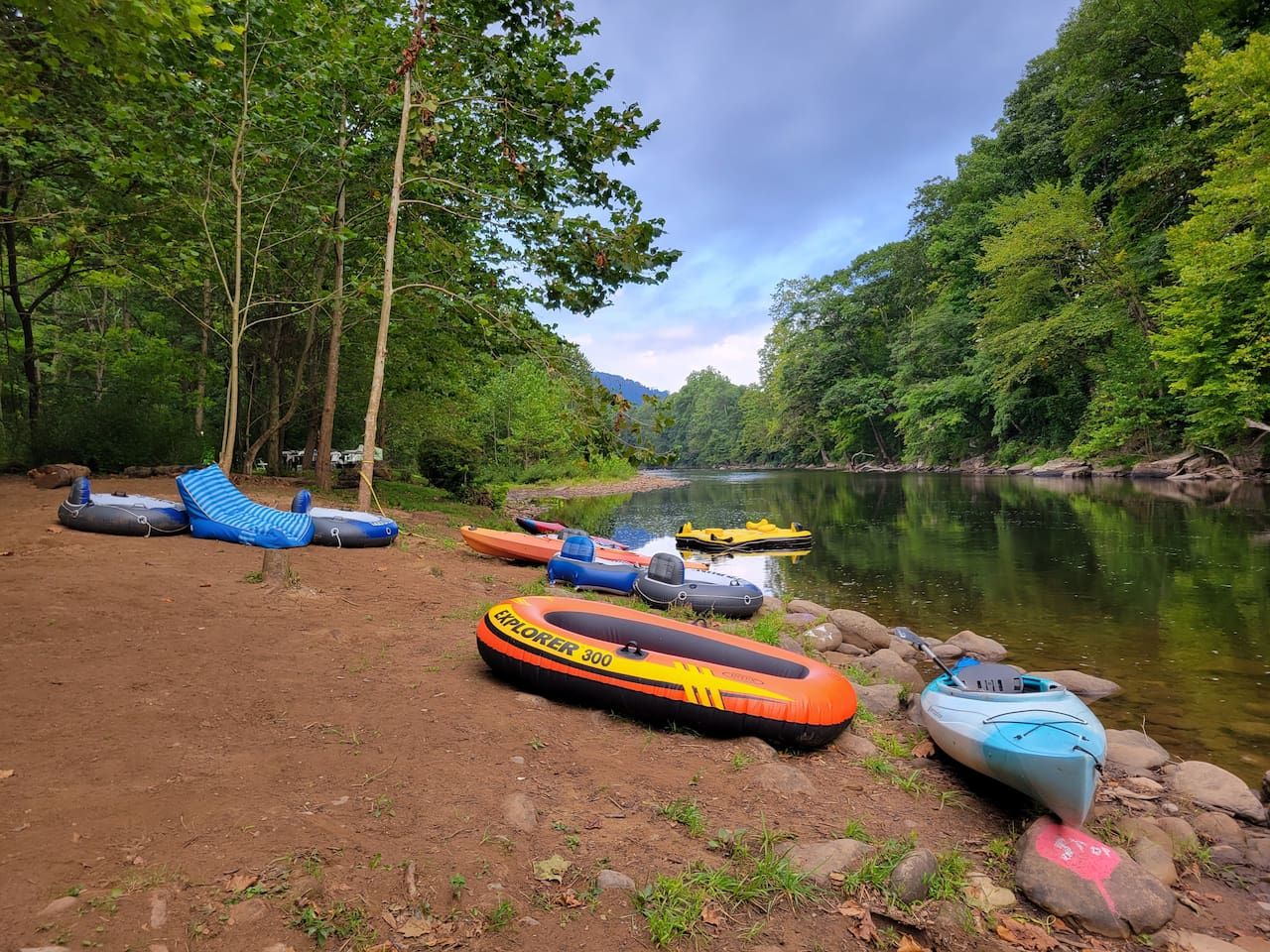 A riverbank with several inflatable rafts and a kayak.