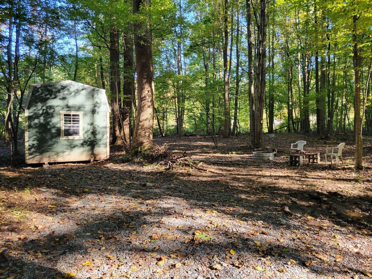 A rustic cabin in a forest with a gravel ground and a small outdoor seating area.